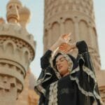 A woman in traditional abaya poses gracefully outside a mosque, embracing spirituality and culture.