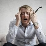 Stressed man sitting on couch, feeling overwhelmed and frustrated, expressing mental strain.