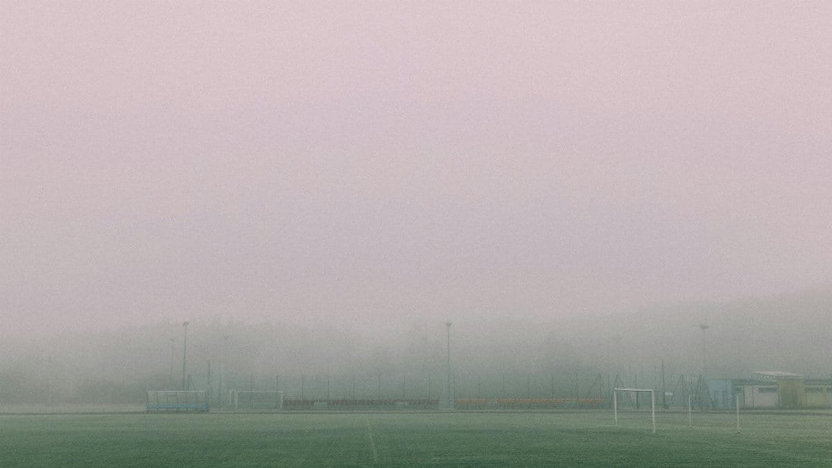 A foggy football field with goals visible, creating a serene and moody winter atmosphere.