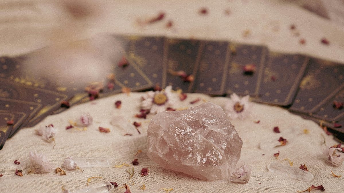Close-up of rose quartz and tarot cards on fabric, surrounded by dried flowers.
