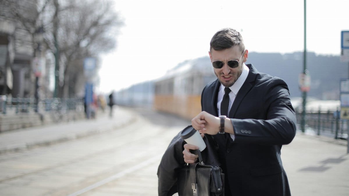 A businessman in a suit checks his watch while rushing on a sunny day in the city.