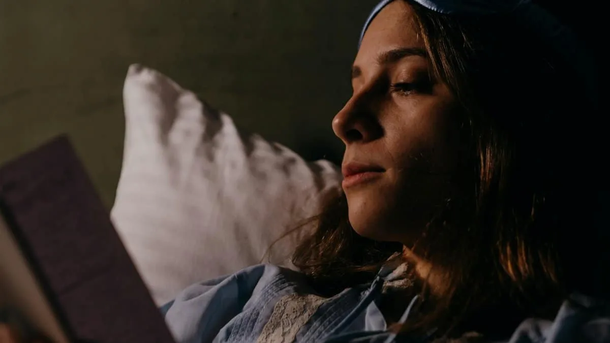 Woman reading in bed with a blue sleep mask, cozy nighttime routine.