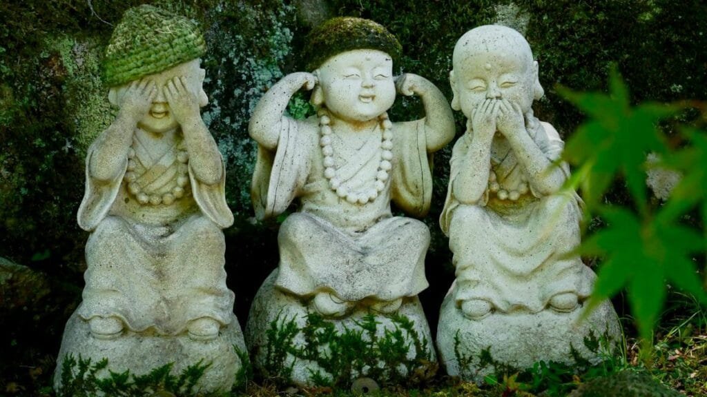 Three wise Buddha statues with moss detail in a peaceful Japanese garden.