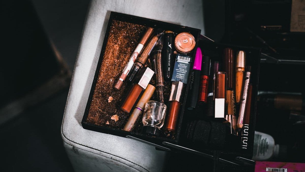 A cluttered cosmetic box filled with assorted makeup items and scattered glitter, capturing a chaotic beauty scene.