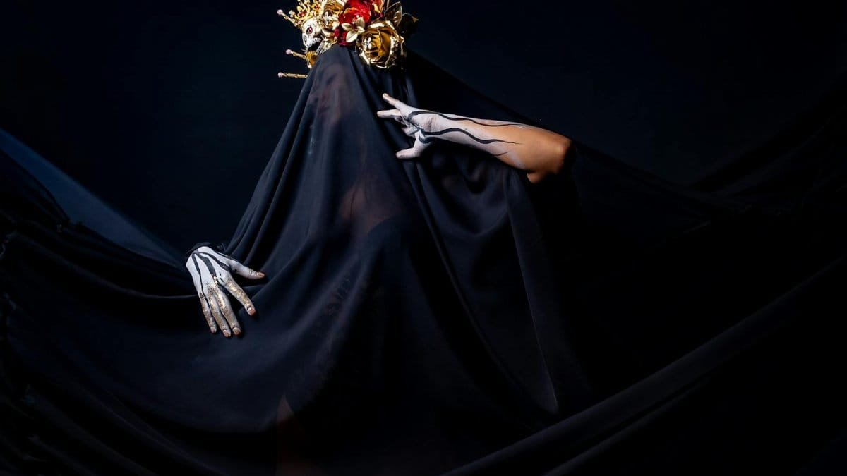 A dramatic portrait featuring a person with a gold headdress and black veil, set against a dark background.