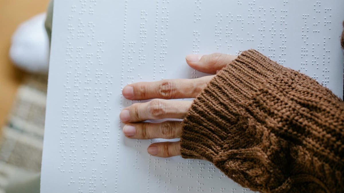 A hand with a knitted sweater touching embossed Braille text on paper.