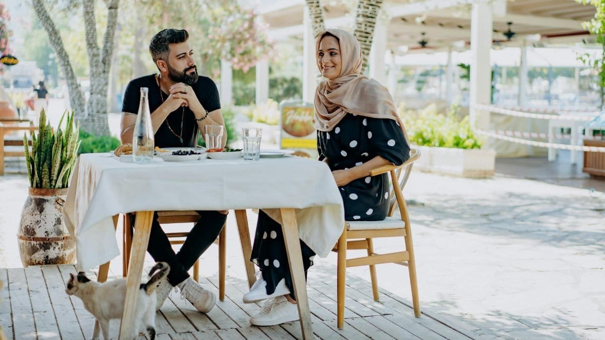 A couple enjoys a relaxed outdoor meal accompanied by a cat, showcasing a summer ambiance.