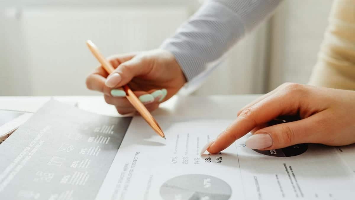 Hands holding a pencil, analyzing charts and data sheets, suggesting teamwork in an office setting.
