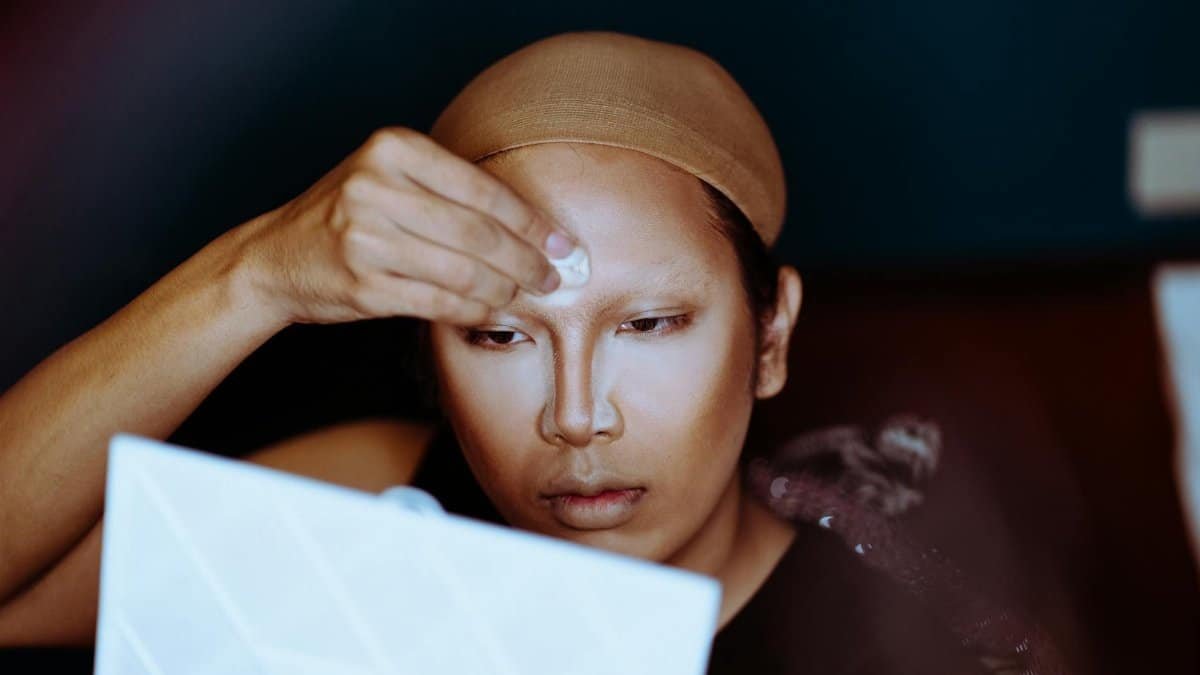 Person in wig cap applying makeup focused on foundation and contouring indoors.