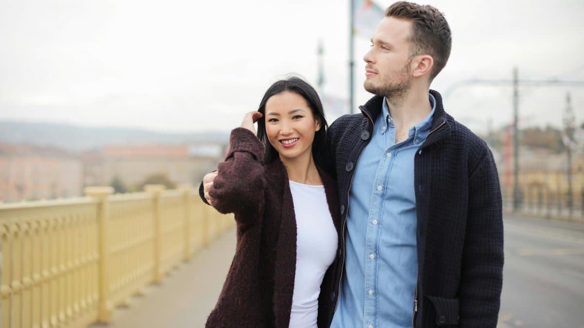 A happy couple walking arm in arm on a sunny day across a city bridge, sharing smiles and affection.