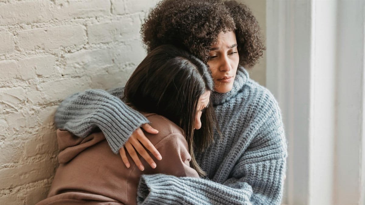 Two friends share an emotional embrace, offering comfort and support indoors.