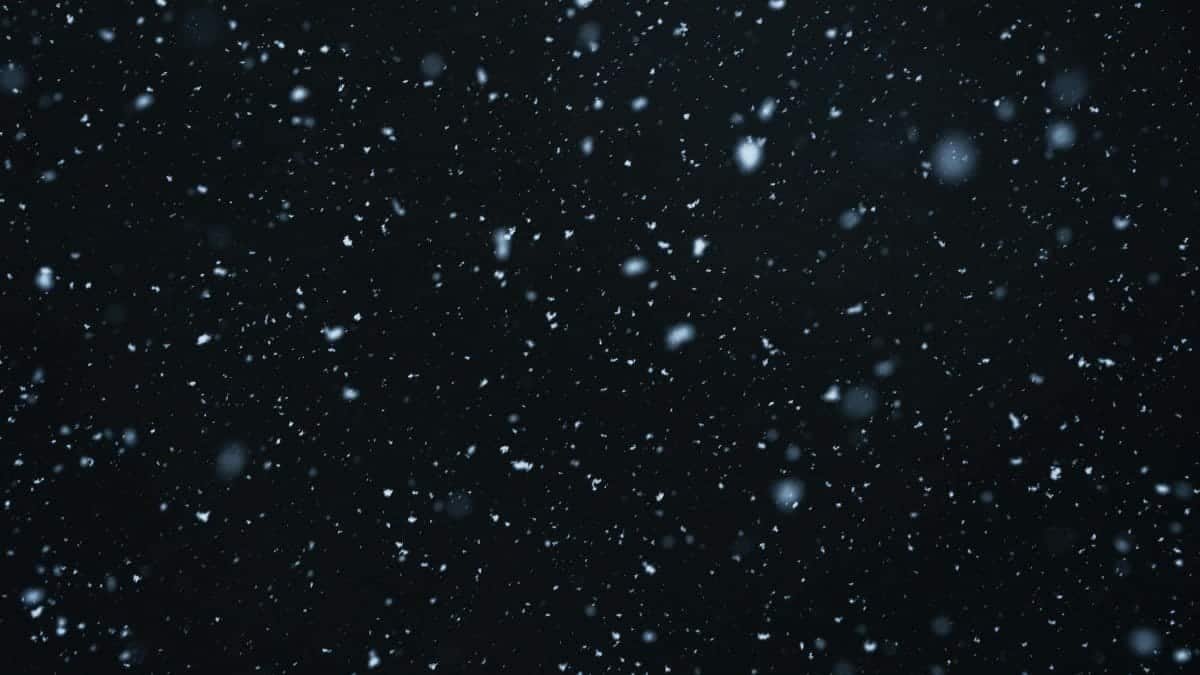 A mesmerizing view of snowflakes falling against a dark, starry night sky.