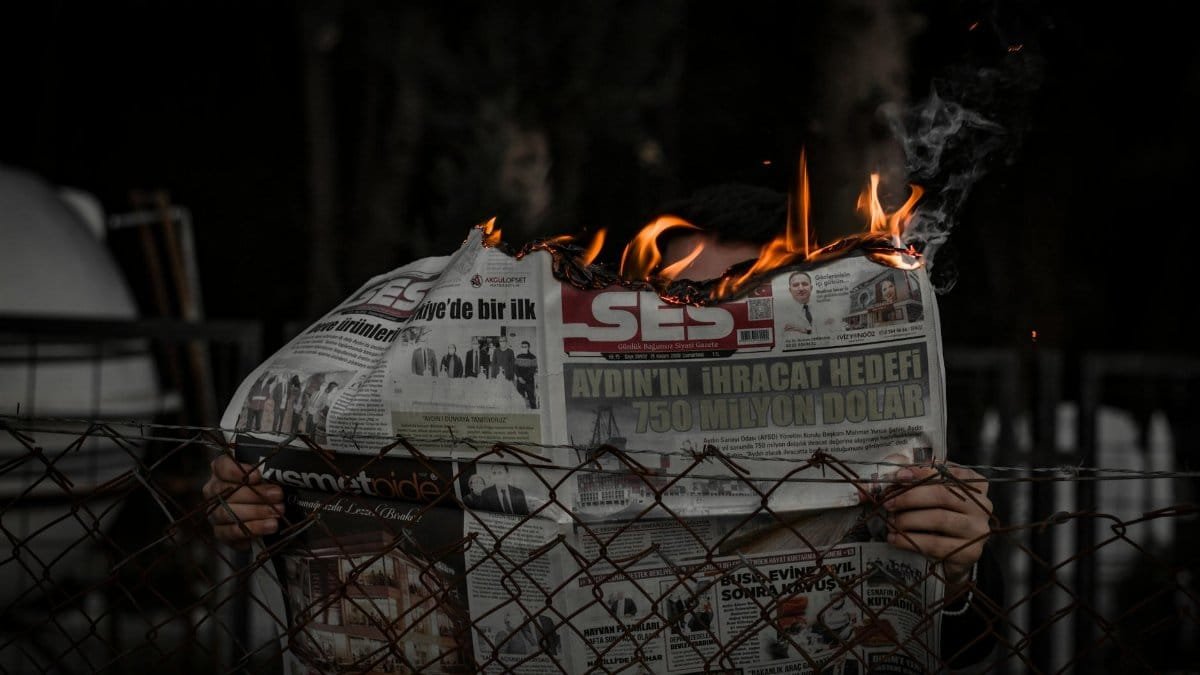 Person holding a burning newspaper outdoors, representing chaos or protest.
