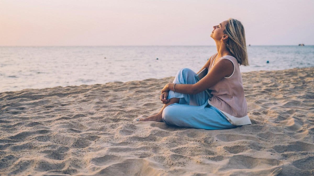 A peaceful moment as a woman relaxes on a sandy beach, enjoying the sunset.