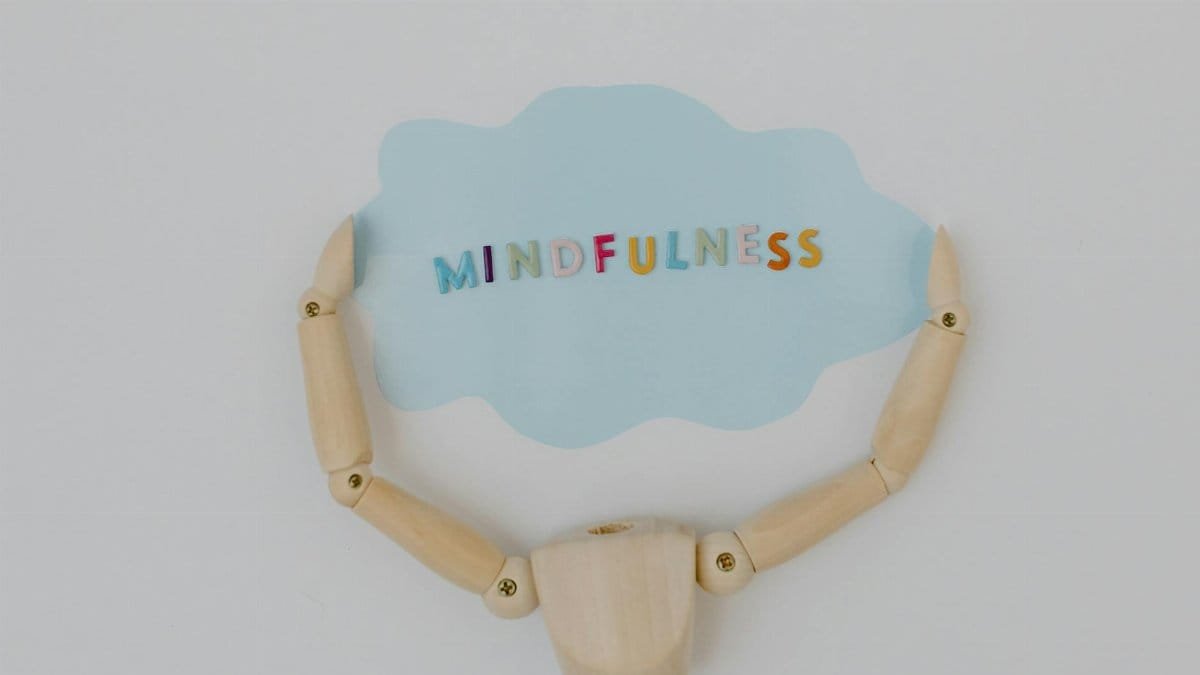 Wooden mannequin arms holding a blue cloud with 'Mindfulness' text, promoting self-awareness.