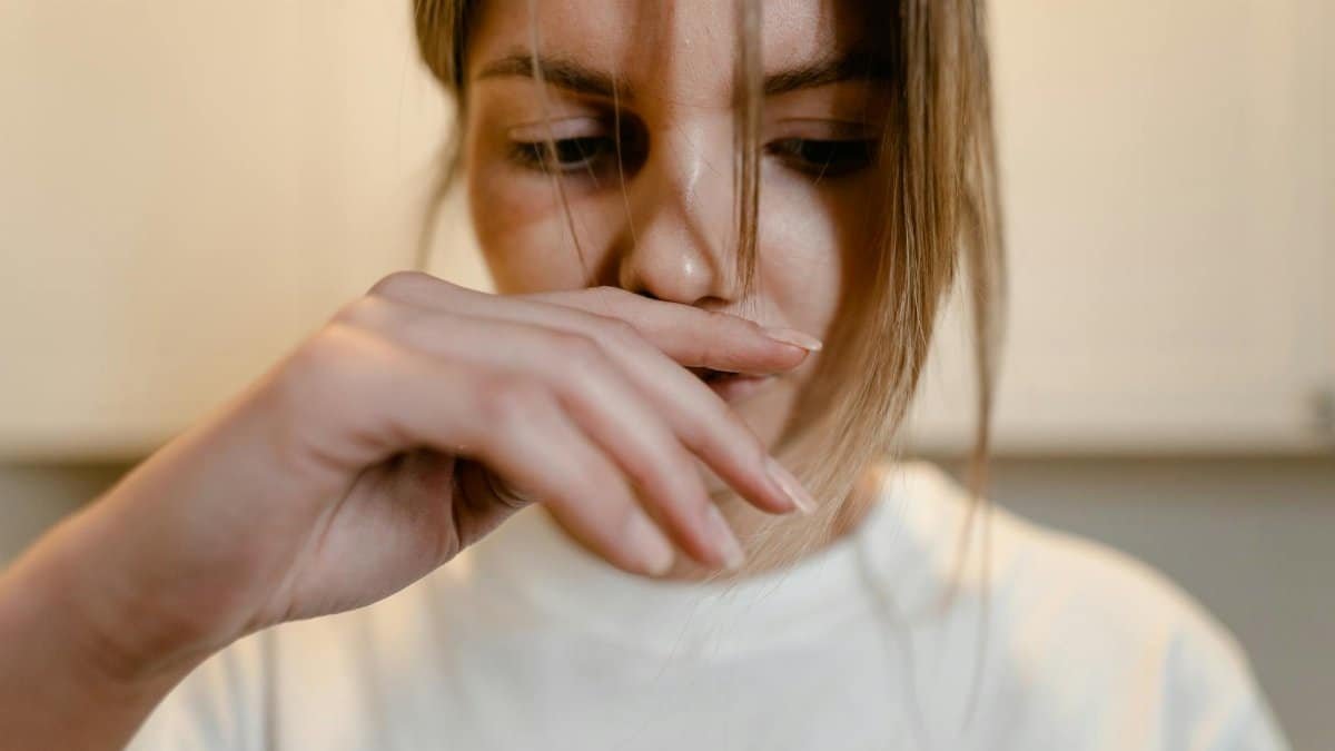 A woman appears deep in thought, with hand over lips, conveying emotional distress.