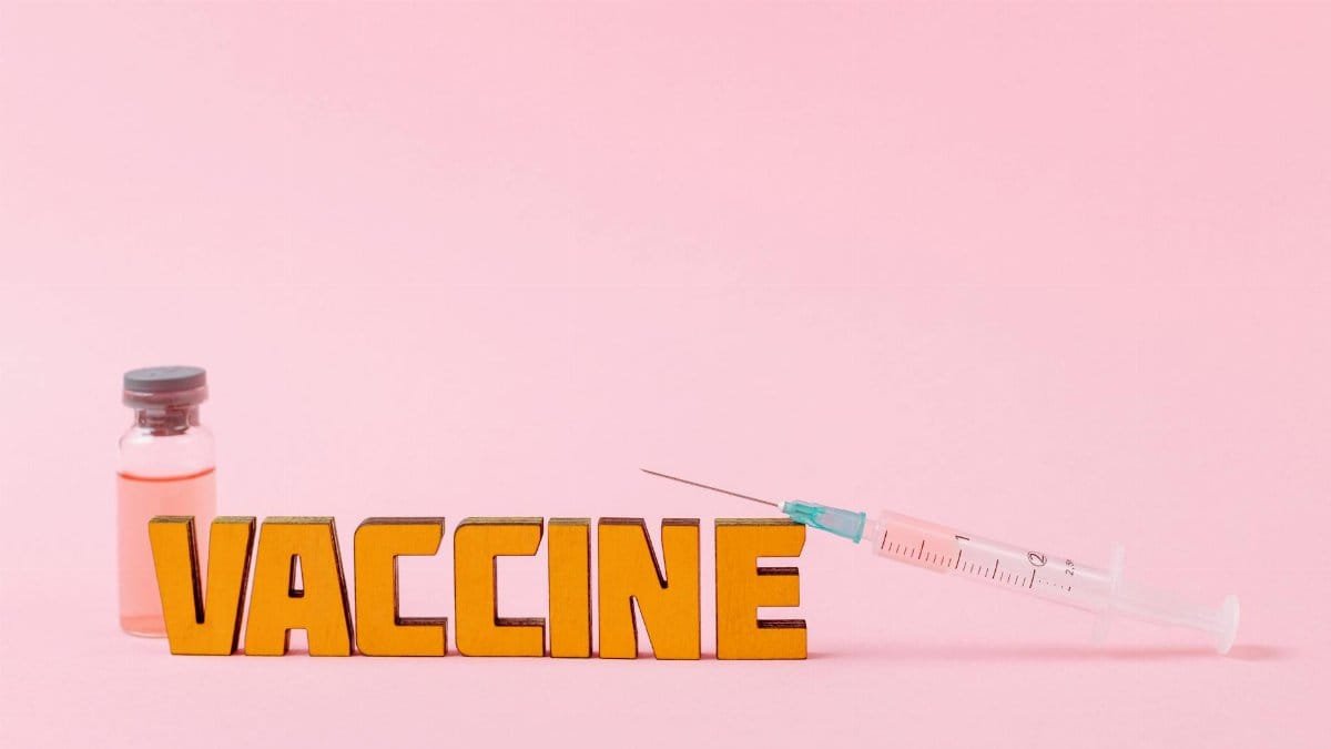 Close-up of a syringe and vaccine vial on a pink backdrop for health concepts.