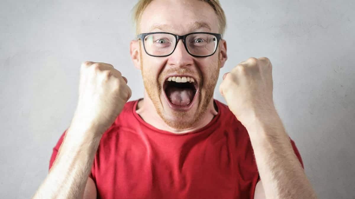 A cheerful man in a red shirt expressing excitement indoors.