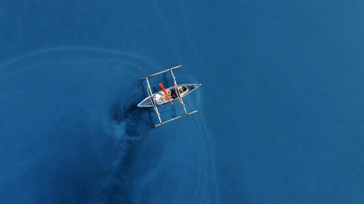 Drone shot of a single boat on the vast blue ocean, highlighting solitude and travel.