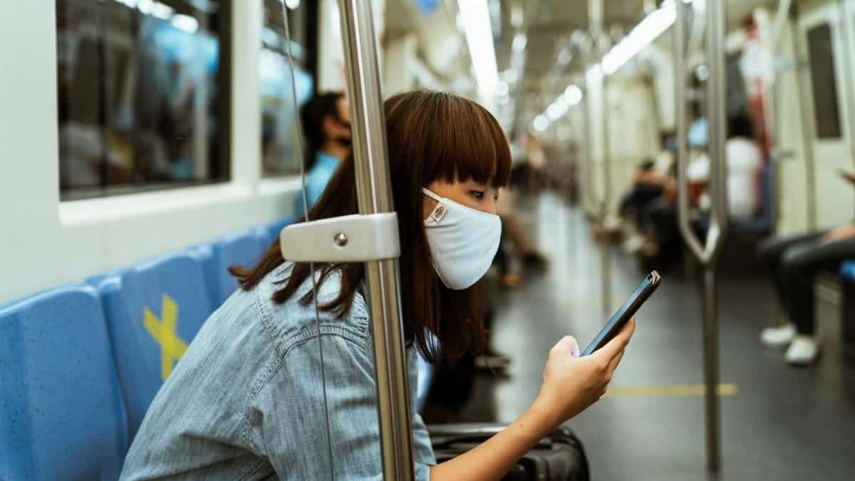Asian woman wearing a face mask, seated in a subway, using smartphone, with focus on modern public transportation.