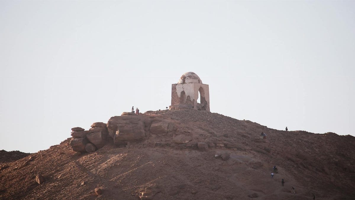 Silhouetted ancient mausoleum atop a desert hill at sunset in Egypt, a serene historical landscape.
