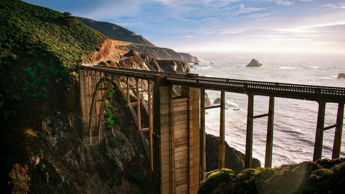 Stunning aerial view of Bixby Creek Bridge against the backdrop of Big Sur's dramatic coastline at sunset.
