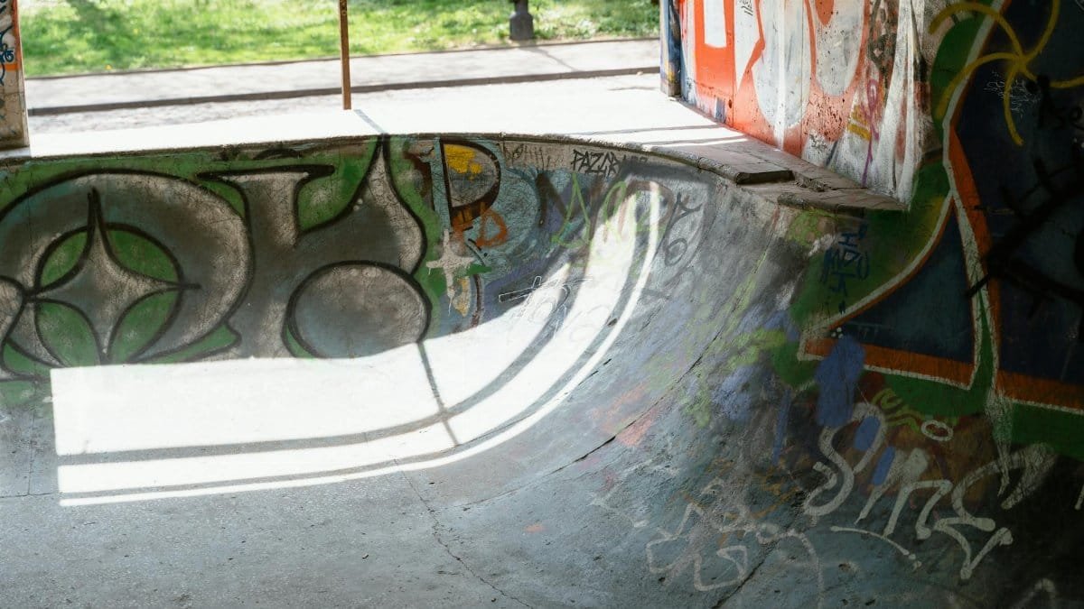 Skate park ramp covered in colorful graffiti art under sunlight.