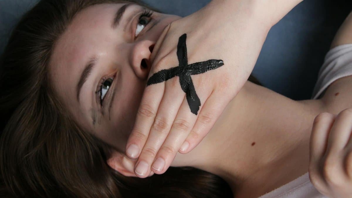 A conceptual portrait of a woman with a marked hand over her mouth, symbolizing silence or censorship.