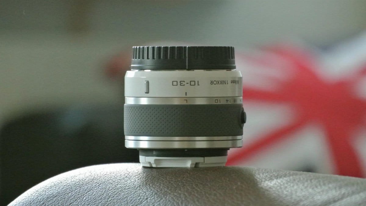 Close-up of a NIKON camera lens resting on a leather surface with a Union Jack background.