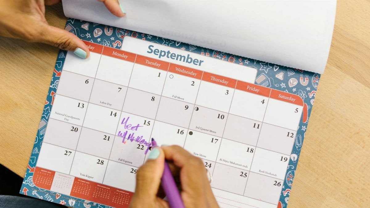 A person marking a calendar in September with a purple pen on a wooden desk.
