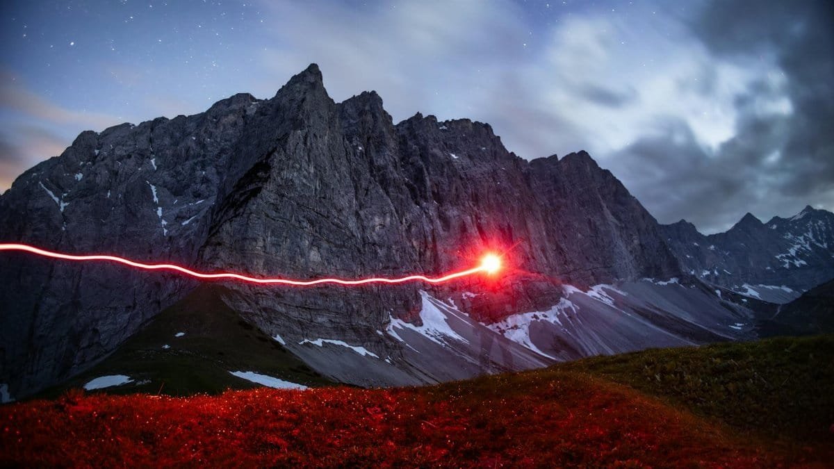 A long exposure captures a mystical red light streak against the majestic Alps at night, revealing a sense of mystery and adventure.