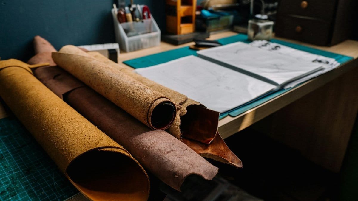 Leather rolls on a workshop desk with tools and sketches, ideal for crafting projects.