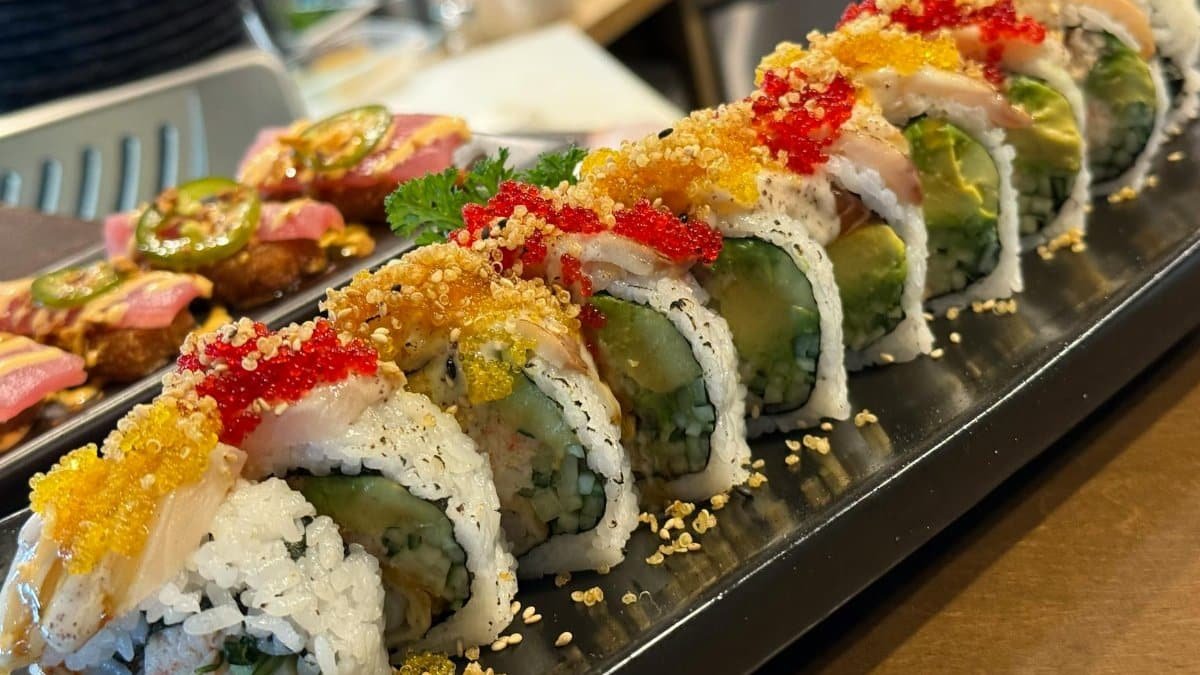 A beautifully arranged gourmet sushi roll with vibrant toppings served on a black platter indoors.