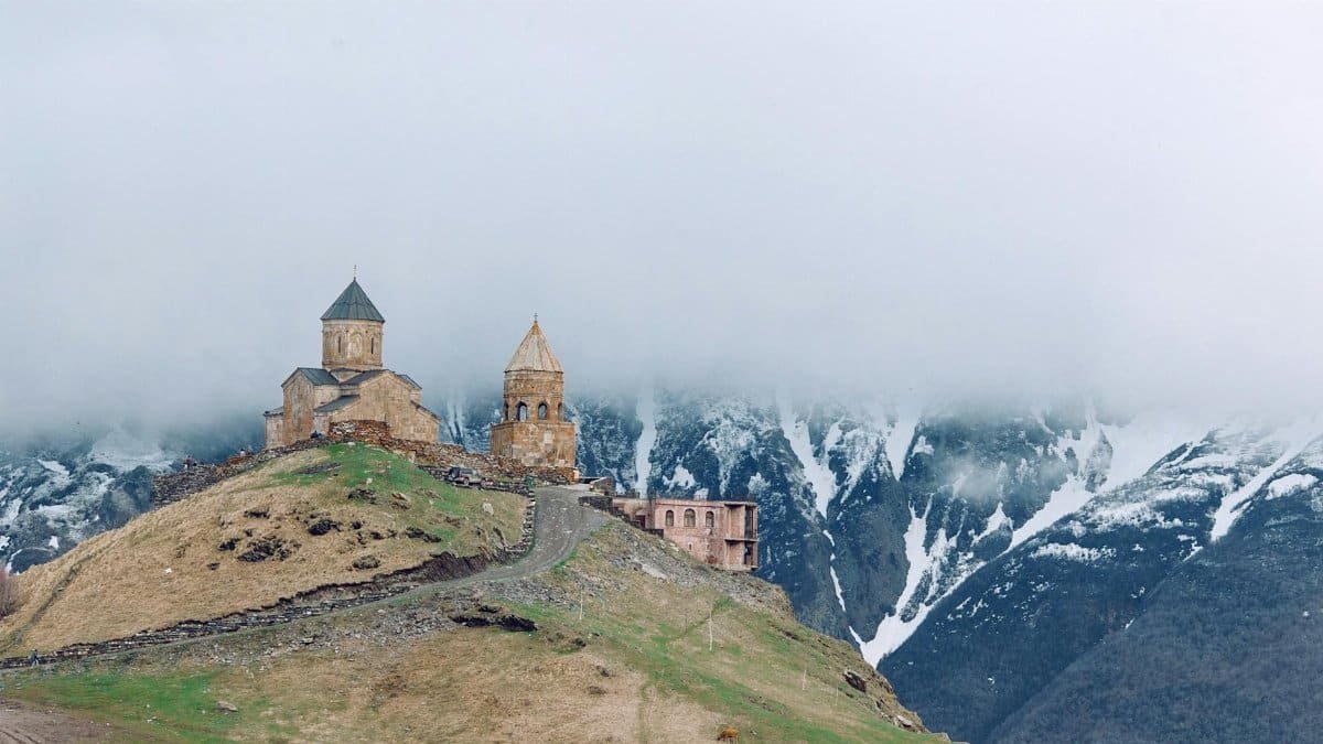 Gergeti Trinity Church atop a hill, shrouded in mist against mountainous backdrop.