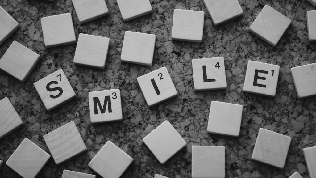 Monochrome image of Scrabble tiles forming the word 'Smile' on a textured surface.