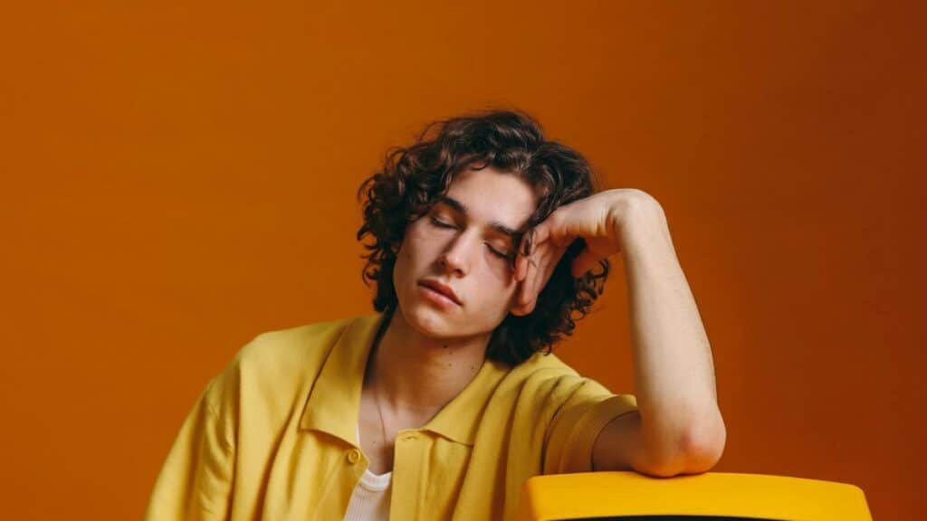 Young man with curly hair in vibrant yellow attire resting on a vintage TV set.