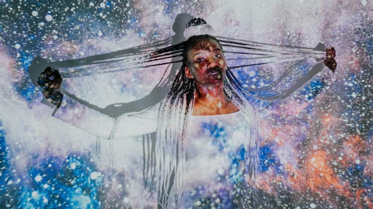 A hauntingly beautiful portrait of a woman with braided hair set against an ethereal starry backdrop.
