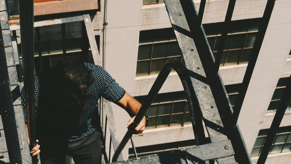 A man climbing a fire escape on a city building on a sunny day.