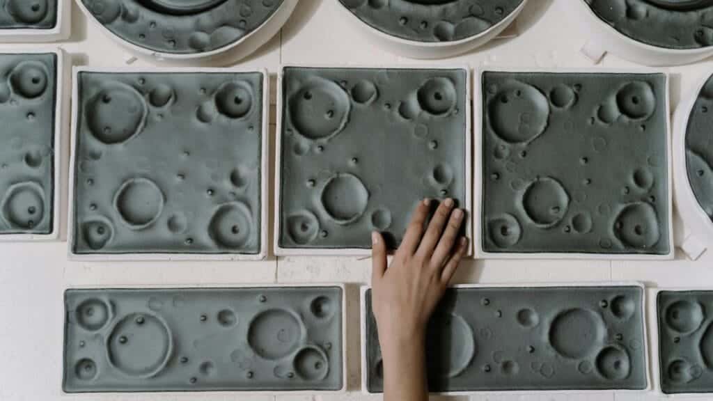 A hand touching handcrafted ceramic plates with unique lunar surface patterns, showcasing craftsmanship.