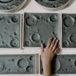A hand touching handcrafted ceramic plates with unique lunar surface patterns, showcasing craftsmanship.