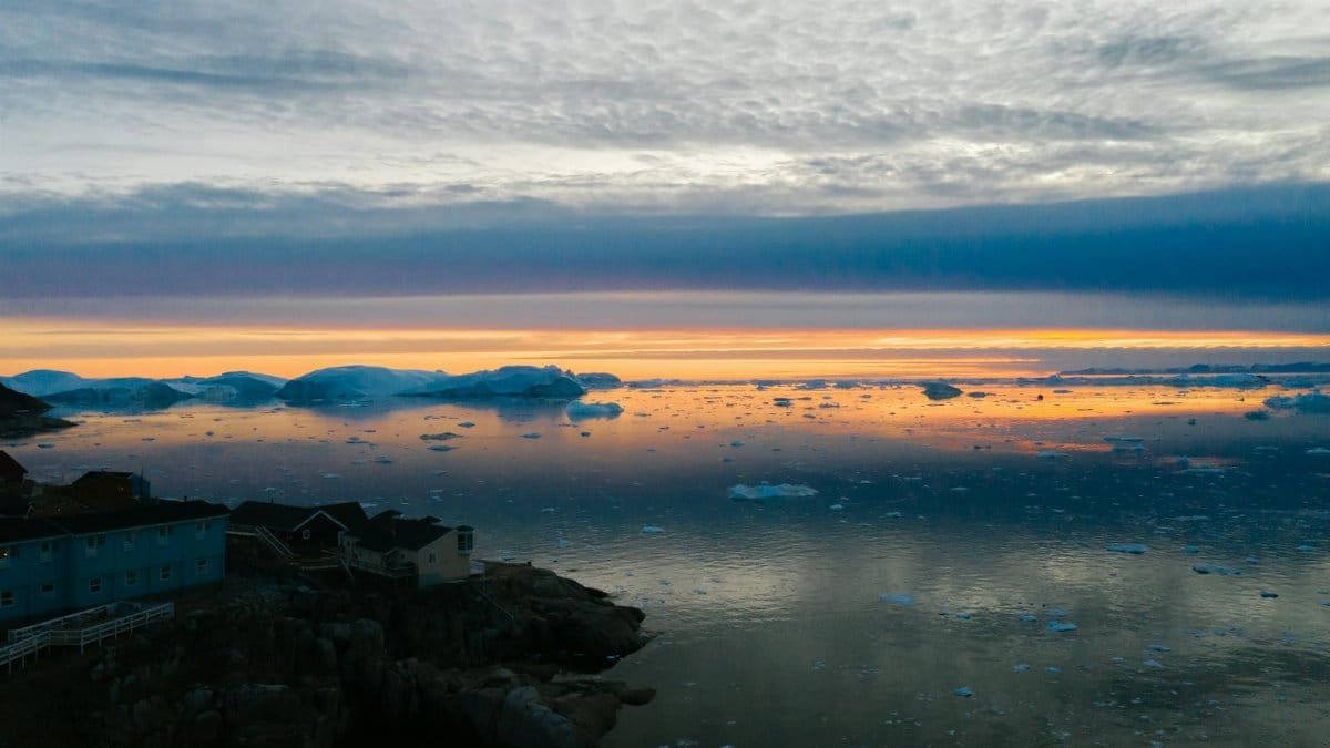 Breathtaking sunset over a coastal village with floating icebergs and calm sea reflections.