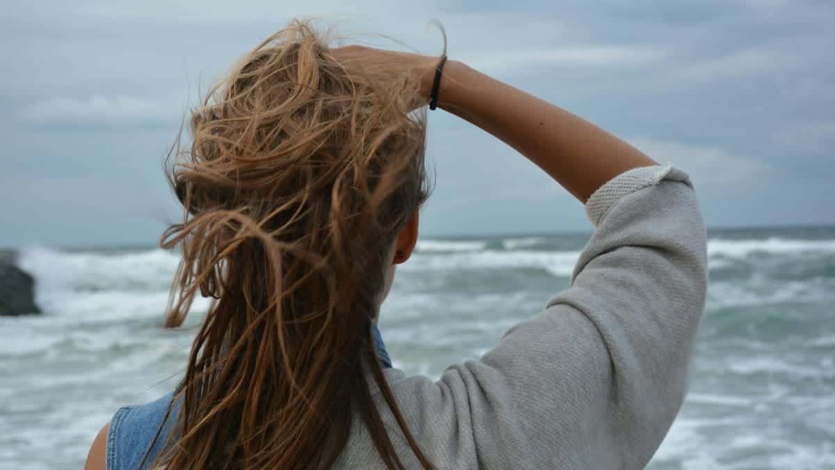 Back view of a young woman with tousled hair observing a windy ocean seascape.