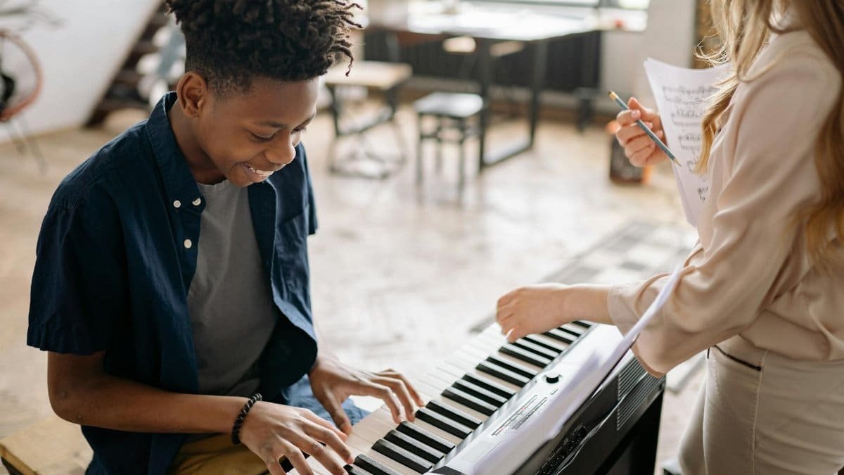A young boy enjoying a piano lesson with a smiling teacher in a cozy indoor setting.