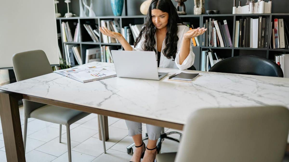 Woman sitting in an office with a laptop, working remotely with a confused expression.