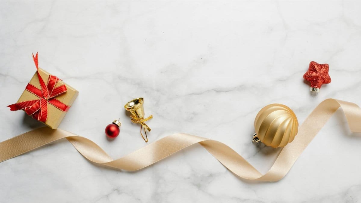Top view of festive Christmas golden bell with bauble and red star near gift box with shiny ribbon on marble