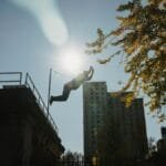 Silhouette of anonymous male athlete performing trick while practicing parkour under bright sunlight