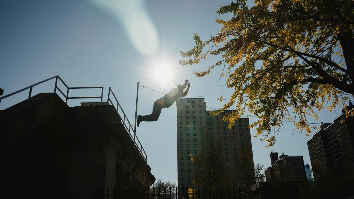 Silhouette of anonymous male athlete performing trick while practicing parkour under bright sunlight