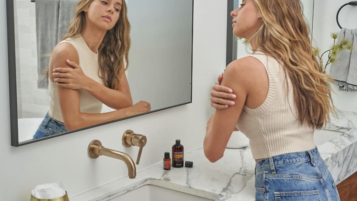 A woman applying essential oils while looking at her reflection in the bathroom mirror.