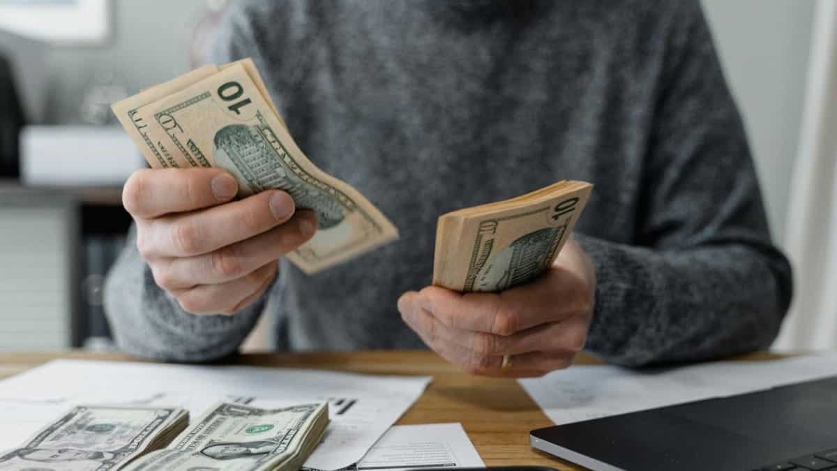 Close-up of person counting cash with a calculator and paperwork on a desk.