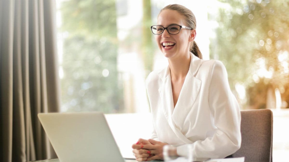 Cheerful businesswoman in glasses working on a laptop, in a bright and modern office setting.